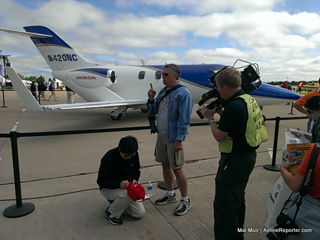 CEO of Hondajet Michimasa Fujino kneels down to sign an autograph on a HondaJet Cap.. yes that really happened - Photo: Mal Muir | AirlineReporter.com