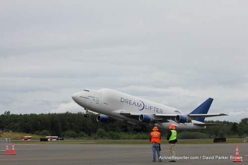 A Boeing 747 Dreamlifter lifts off as volunteers watch. Notice the classic bi-planes (which guests could pay to fly on) in the background.