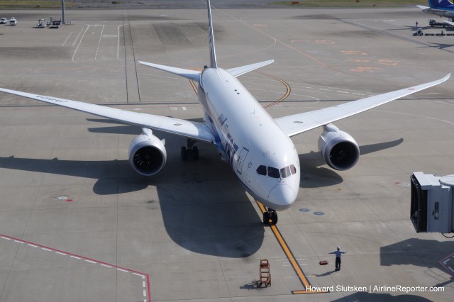 An ANA 787 approaching the gate, marshalled by what looks like a Lego Minifig (giant size)