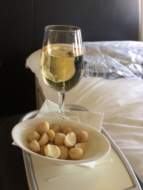 A glass of champagne with some macadamia nuts. Also, a glimpse of the wonderful bed. Photo - Bernie Leighton | AirlineReporter.com