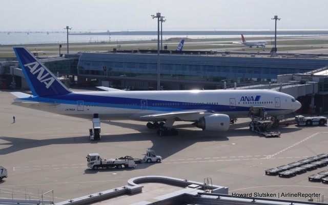 On the ramp at Tokyo-Haneda, an ANA Boeing 777-200 with pod-loader, belt loader, towbar tractor by the plane, and lavatory service truck going by.