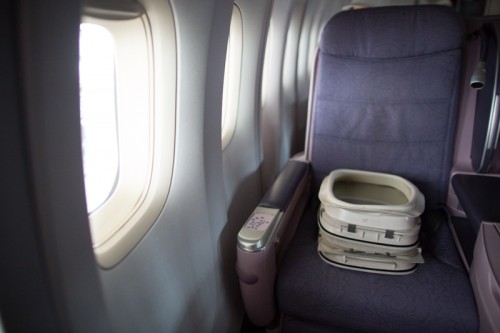 A pair of interior window frames rest on a business class seat in the nose of a 747 in progress.