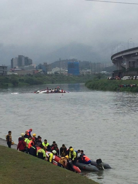 Rescuers and passengers can be seen on the bank with the TransAsia ATR72 in the background - Photo: Yung Jen