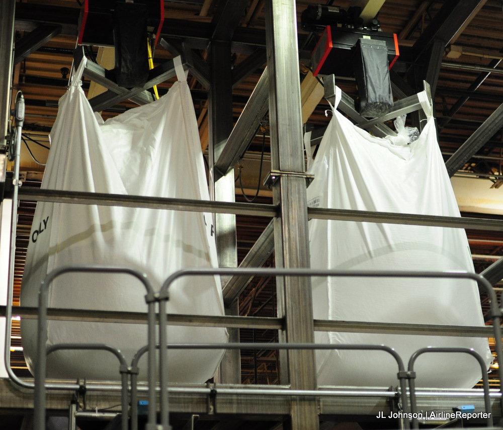 Two 1-ton sacks of peanuts hang above proprietary machinery awaiting processing