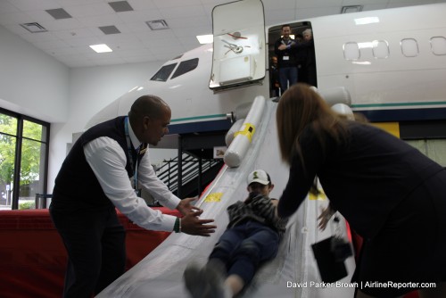 A Boy Scout member slides down, with flight attendants helping out