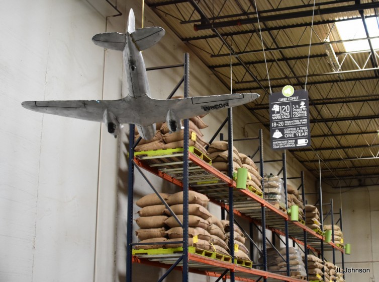 Burlap sacks of green (unroasted} coffee line the walls. Note the DC-3 model. 