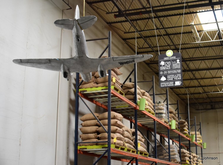 Burlap sacks of green (unroasted} coffee line the walls. Note the DC-3 model.