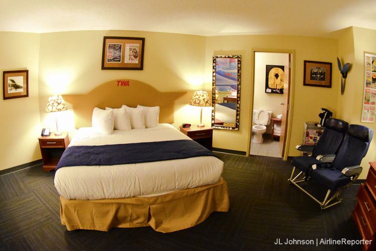 A balanced and tastefully decorated TWA-themed room complete with airplane seats. 