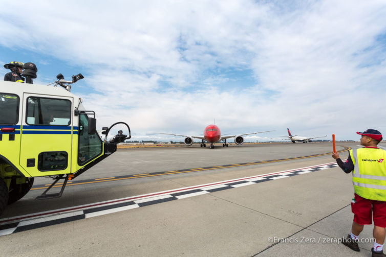 A Port of Seattle firefighter and a ramp worker prepare watch as the jet rolls up to its stand.