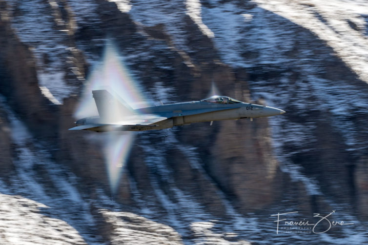 An F/A-18 flirting with the sound barrier. Notice the visible shock waves distorting the slightly humid air over the cockpit and beneath the fuselage.