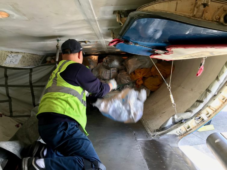 Alaska Airlines Ramp Service Agent (RSA) Carlos Arenas, foreground, passes a bag of mail to Lead RSA Metin Mehmedov. Both are working in the aft belly hold of the aircraft.