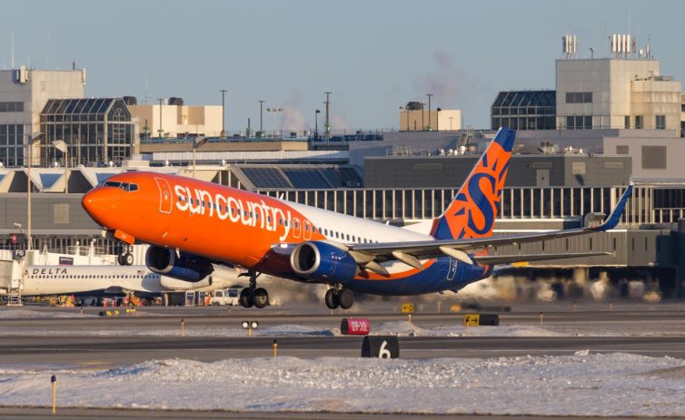 A tide pod livery 737 jets down the runway with exhaust causing amazing distortion. There's snow in the foreground and you can see steam from ventilation or heater exhaust in the background. The lighting is excellent, everything is warm. 