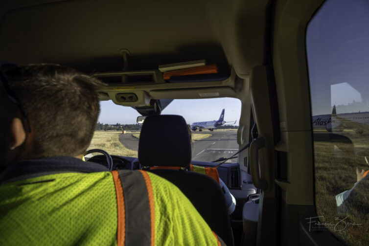 A photo from inside of a vehicle, looking out toward an airplane taxiing at SEA airport