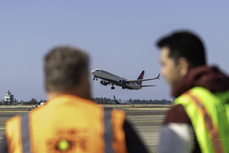 A Delta 737 takes off, framed by two avgeeks